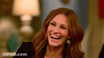 A Woman Is Laughing And Smiling While Sitting At A Table . GIF