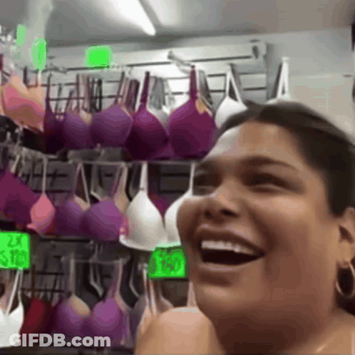 A Woman Is Laughing In Front Of A Display Of Purple And White Bras GIF