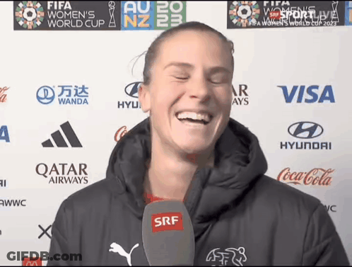 A Woman Is Laughing In Front Of A Wall With Logos For Qatar Airways Coca Cola And Visa GIF
