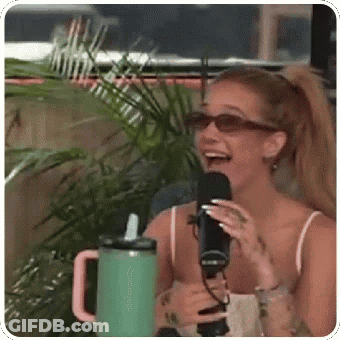 A Woman Is Laughing While Holding A Microphone In Front Of A Green Cup . GIF