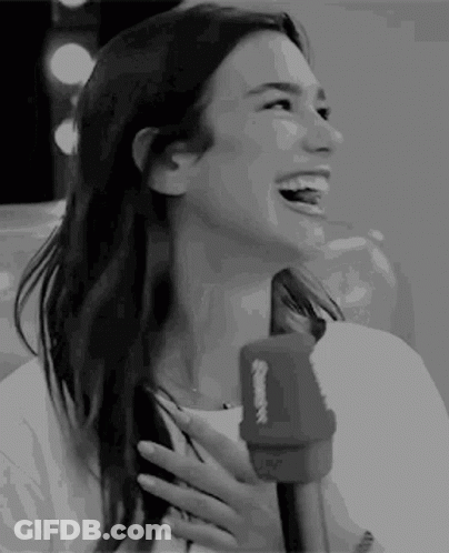 A Woman Is Laughing While Holding A Microphone In Her Hand . GIF