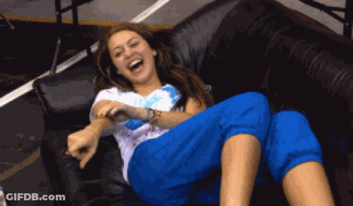 A Woman Is Laughing While Laying On A Couch With Her Legs Crossed GIF