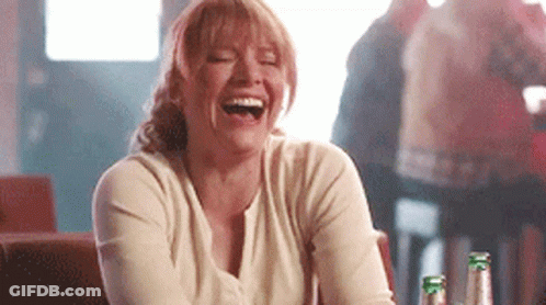 A Woman Is Laughing While Sitting At A Table In A Bar . GIF