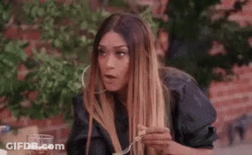 A Woman Is Laughing While Sitting At A Table With A Glass Of Whiskey In Her Hand . GIF