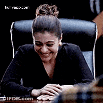 A Woman Is Laughing While Sitting At A Table With Her Hands On Her Lap . GIF
