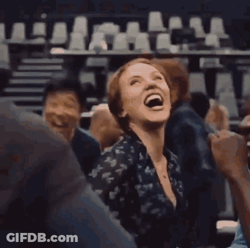 A Woman Is Laughing While Sitting In A Crowd Of People In A Theater . GIF
