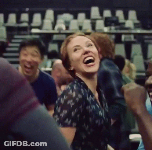 A Woman Is Laughing While Sitting In A Crowd Of People . GIF