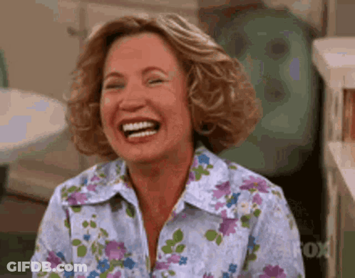 A Woman Is Laughing While Wearing A Floral Shirt And Smiling . GIF