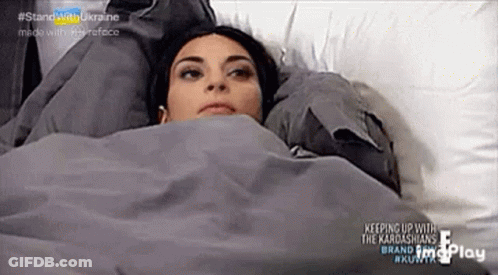 A Woman Is Laying In A Bed Under A Blanket And Looking Up . GIF