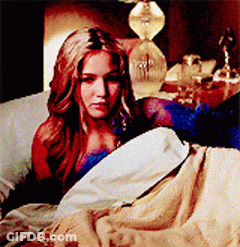 A Woman Is Laying In A Bed With A Lamp In The Background GIF