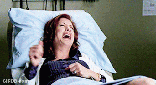 A Woman Is Laying In A Hospital Bed Laughing With Her Eyes Closed GIF