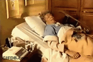 A Woman Is Laying In A Hospital Bed With A Blanket On . GIF