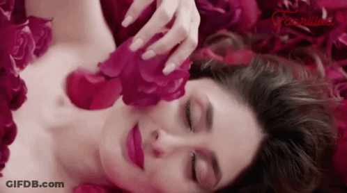 A Woman Is Laying In A Pile Of Pink Rose Petals GIF
