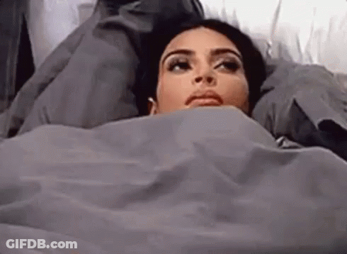 A Woman Is Laying In Bed Covered In A Blanket . GIF