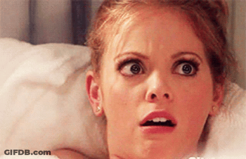 A Woman Is Laying In Bed Making A Surprised Face . GIF