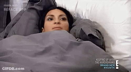 A Woman Is Laying In Bed Under A Blanket With Her Head On A Pillow . GIF