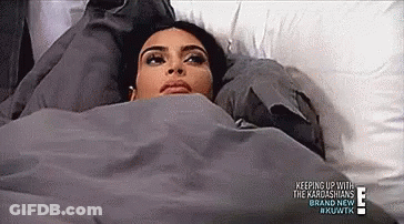 A Woman Is Laying In Bed Under A Blanket With Her Head On A Pillow . GIF