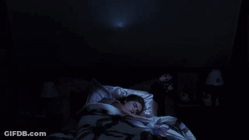 A Woman Is Laying In Bed With A Ghost Coming Out Of The Ceiling Above Her . GIF