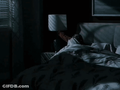 A Woman Is Laying In Bed With A Lamp On The Nightstand Next To Her . GIF