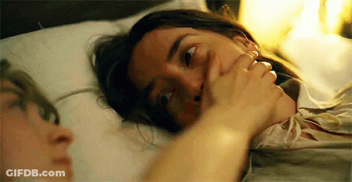 A Woman Is Laying In Bed With A Man Covering Her Mouth With Her Hand . GIF
