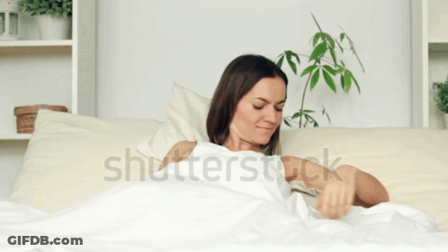 A Woman Is Laying In Bed With Her Arms Outstretched And The Word Shutterstock Is On The Bottom GIF
