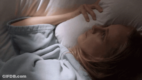 A Woman Is Laying In Bed With Her Hand On Her Forehead GIF