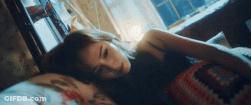 A Woman Is Laying In Bed With Her Head On A Pillow Looking At The Camera . GIF
