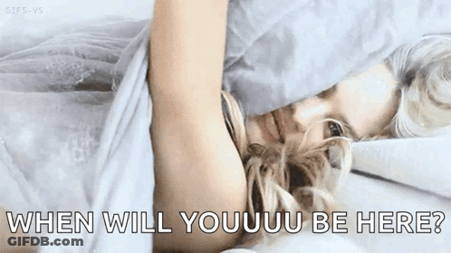 A Woman Is Laying In Bed With The Words `` When Will Youuu Be Here '' Written On The Bottom Of The Image . GIF