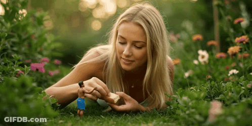 A Woman Is Laying In The Grass Playing With A Toy Man GIF