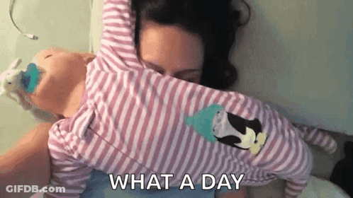 A Woman Is Laying On A Bed Holding A Baby In Her Arms And Says `` What A Day '' . GIF