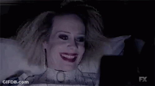 A Woman Is Laying On A Bed Looking At A Cell Phone In A Dark Room . GIF