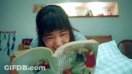 A Woman Is Laying On A Bed Reading A Book And Smiling . GIF