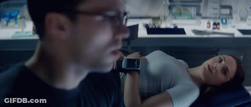 A Woman Is Laying On A Bed While A Man Looks At Her Watch GIF
