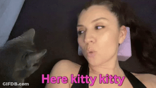 A Woman Is Laying On A Bed With A Cat Looking At Her And Says `` Here Kitty Kitty '' . GIF