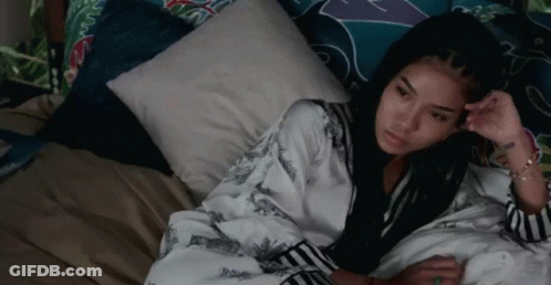 A Woman Is Laying On A Bed With A Pillow And Looking At The Camera . GIF