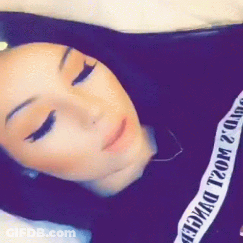 A Woman Is Laying On A Bed With Her Eyes Closed And Wearing A Black Shirt With A White Stripe On It . GIF