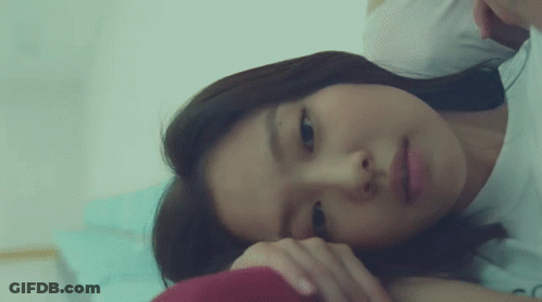 A Woman Is Laying On A Bed With Her Head On Her Hand GIF