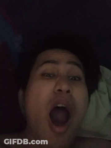 A Woman Is Laying On A Bed With Her Mouth Open And Her Tongue Sticking Out . GIF