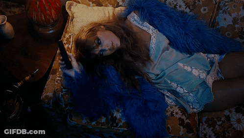 A Woman Is Laying On A Couch Wearing A Blue Fur Coat GIF