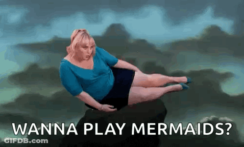 A Woman Is Laying On A Rock With The Words `` Wanna Play Mermaids ? '' Written Below Her . GIF