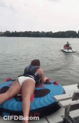 A Woman Is Laying On A Tube In The Water With A Jet Ski Behind Her . GIF
