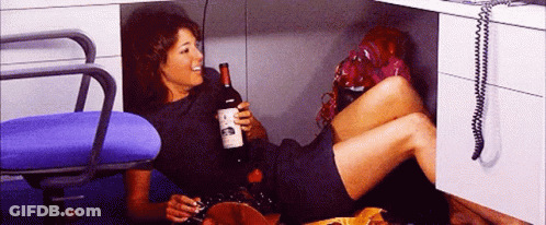 A Woman Is Laying On The Floor Holding A Bottle Of Wine And A Cigarette GIF