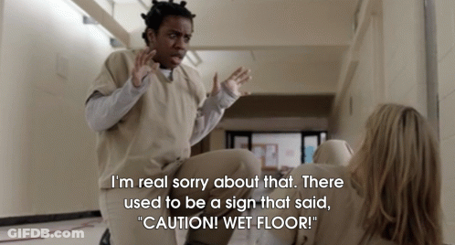 A Woman Is Laying On The Floor With A Sign That Says " Caution Wet Floor " GIF