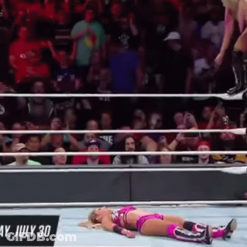 A Woman Is Laying On The Ground In A Wrestling Ring While A Man Jumps Over Her . GIF
