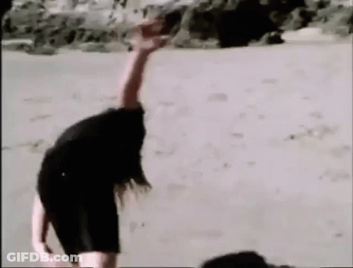 A Woman Is Laying On The Sand With Her Arms Outstretched . GIF