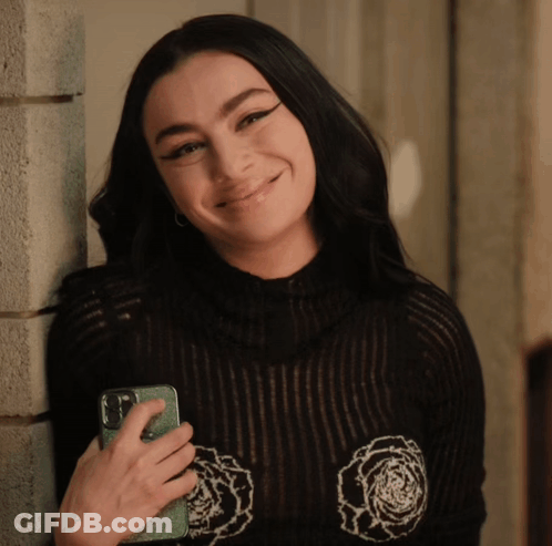 A Woman Is Leaning Against A Wall Holding A Cell Phone GIF