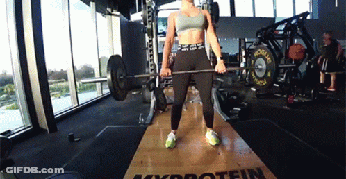A Woman Is Lifting A Barbell In A Gym That Has The Word Protein On The Floor GIF