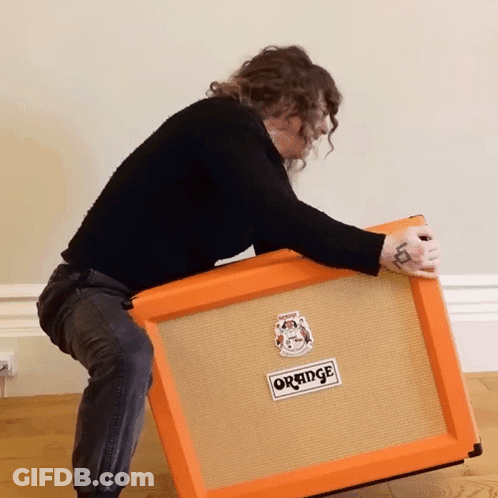 A Woman Is Lifting An Orange Amplifier On Her Knees GIF