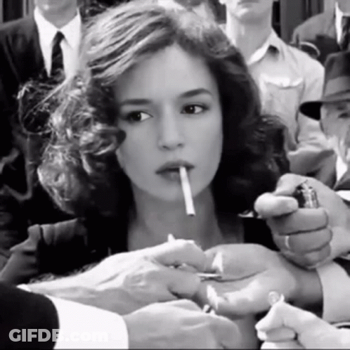 A Woman Is Lighting A Cigarette In A Crowd Of People GIF