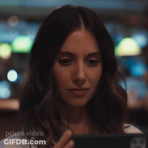 A Woman Is Looking At A Cell Phone In A Restaurant . GIF